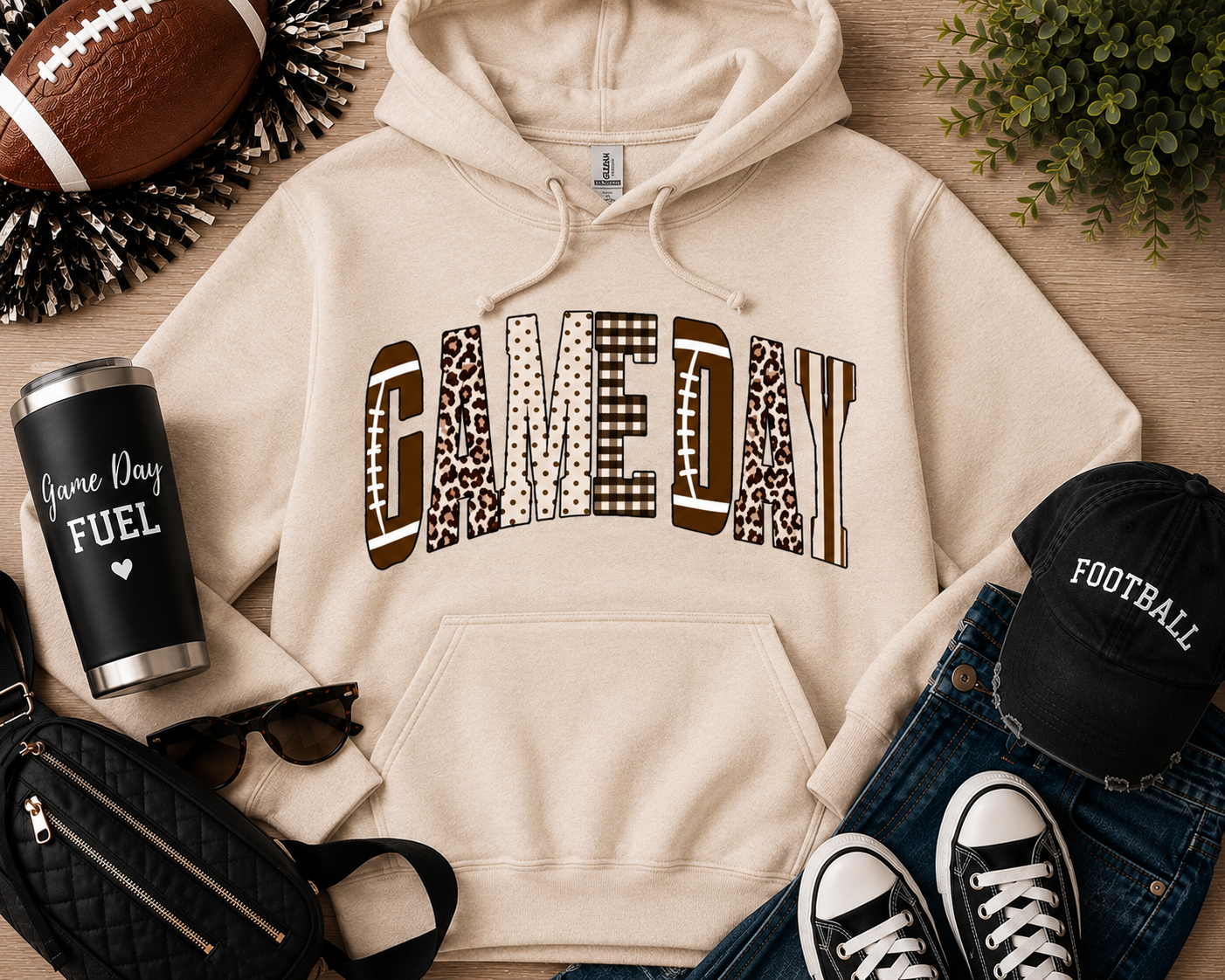 Neutral cream Game Day graphic hoodie featuring varsity-style lettering with football, leopard, gingham, polka dot, and striped patterns. Cozy unisex pullover sweatshirt styled with jeans and football accessories, perfect for tailgates, football season, and fall game day outfits.