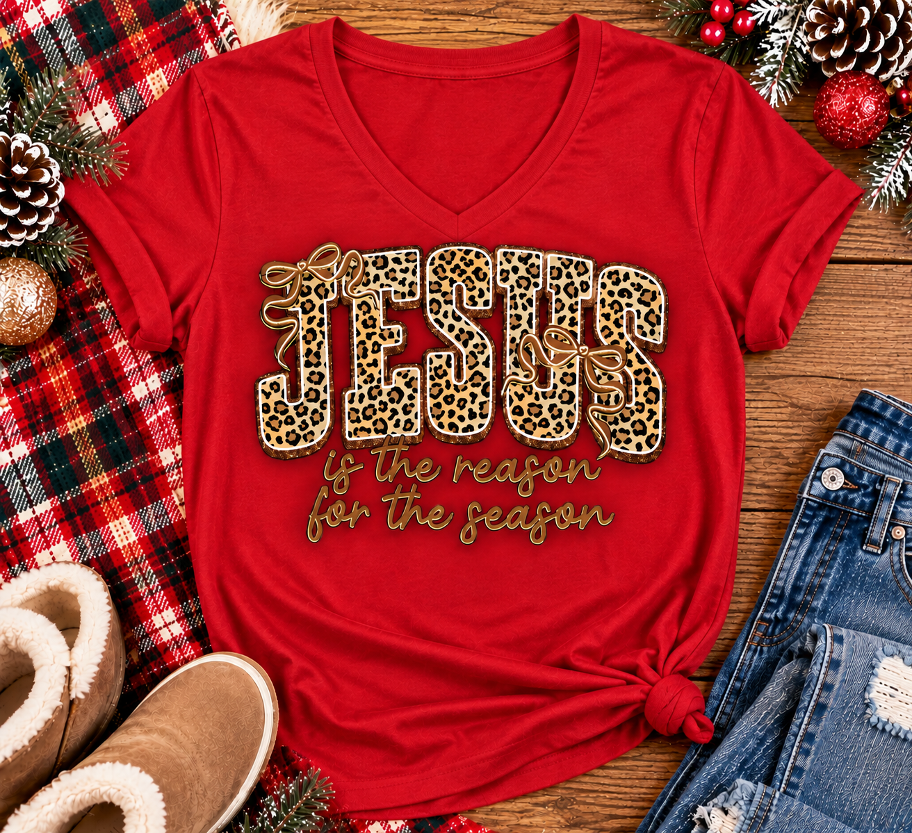 Jesus Is the Reason for the Season Christmas graphic shirt featuring bold leopard print JESUS lettering, decorative gold bows, and gold script. Faith-inspired holiday apparel available in red and black with four style options.