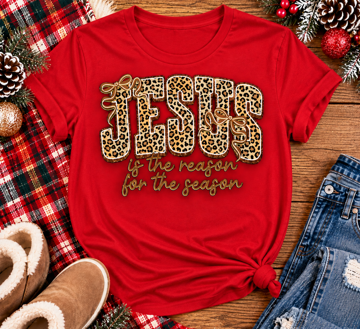 Jesus Is the Reason for the Season Christmas graphic shirt featuring bold leopard print JESUS lettering, decorative gold bows, and gold script. Faith-inspired holiday apparel available in red and black with four style options.